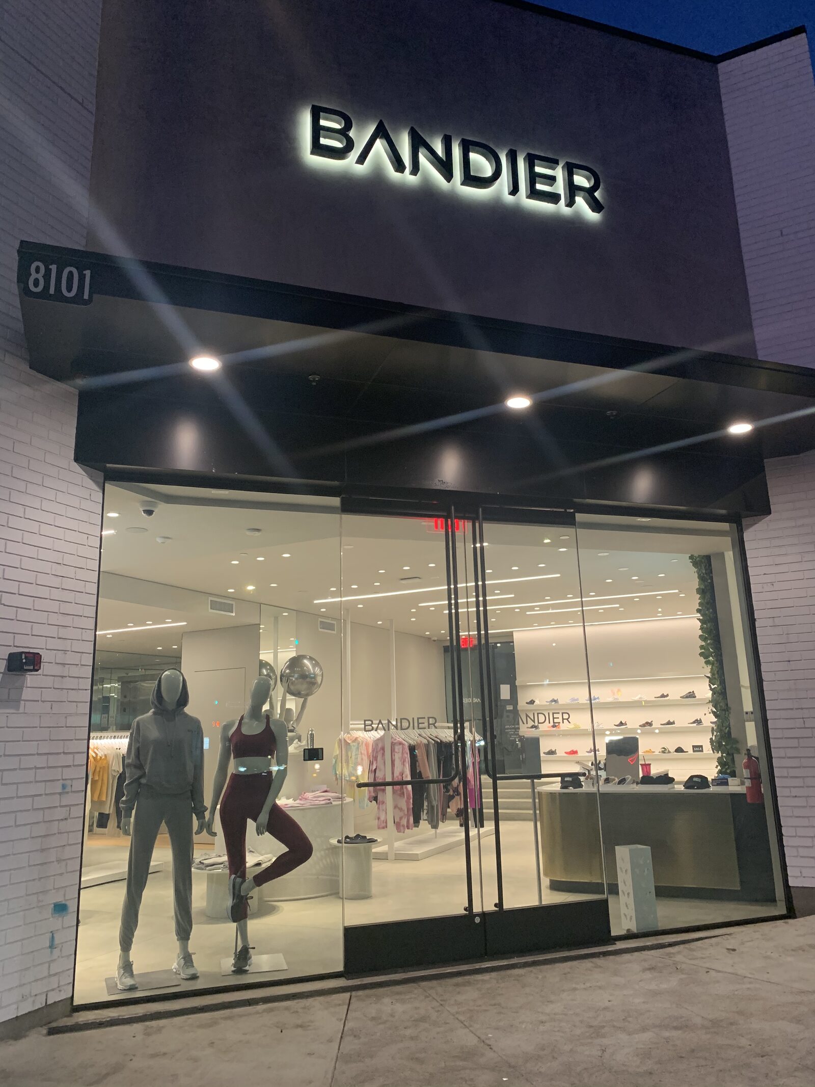 Bandier Los Angeles storefront at night with an illuminated sign, glass entrance, mannequins, and activewear displays.